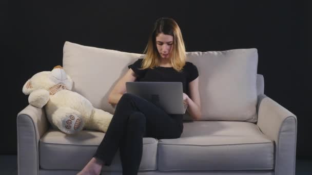Chica con un portátil en el sofá. fondo negro — Vídeos de Stock
