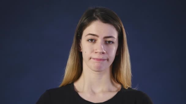 Een leuke jonge witte vrouw kijkt in de camera op een zwarte achtergrond — Stockvideo