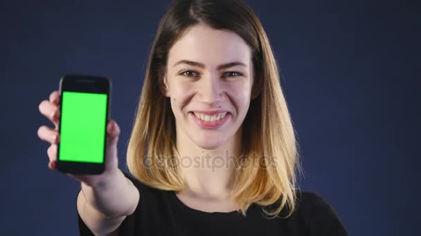 携帯電話に焦点を当てます。若い女性の手の空スマート フォン画面で緑の背景に分離され、画面上を指して見せて — ストック動画