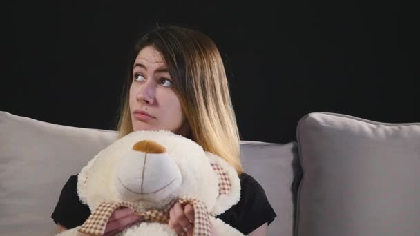 Досить усміхнена жінка сидить на дивані обіймаючи плюшевого ведмедя — стокове відео
