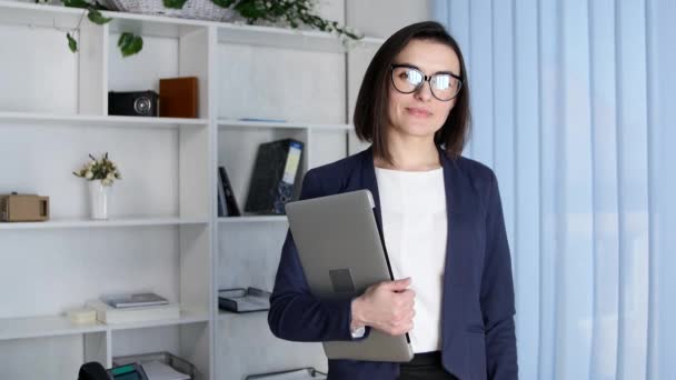 Mujer de negocios sosteniendo un portátil mirando a la cámara — Vídeo de stock