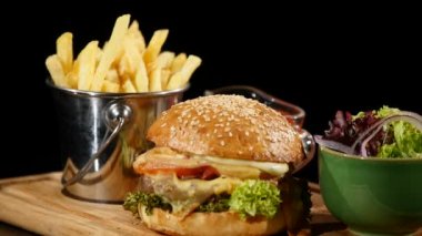 Hamburger ketçap ile dönen patates kızartması ve salata dökülür. Siyah arka plan Hamburger patates kızartması ve salata ile