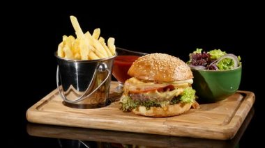 Hamburger ketçap ile dönen patates kızartması ve salata dökülür. Siyah arka plan Hamburger patates kızartması ve salata ile