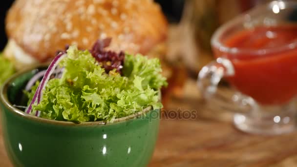 Hambúrguer rotativo com ketchup derramado sobre batatas fritas e salada. Preto fundo Hambúrguer com batatas fritas e salada — Vídeo de Stock