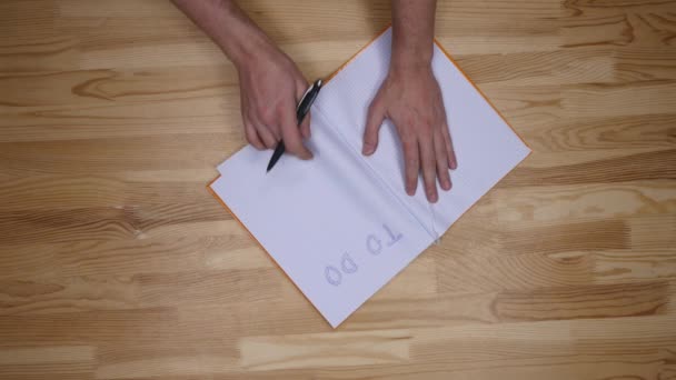 Man hand skrivande att göra-lista på anteckningsblock, ovanifrån — Stockvideo