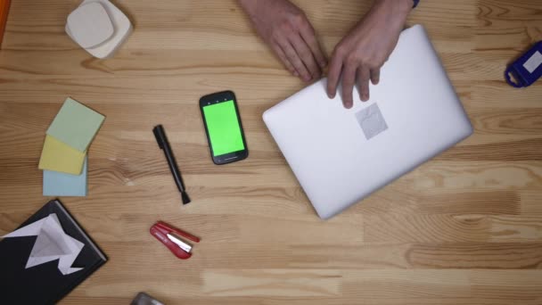 Met behulp van Android telefoon en laptop die leggen op houten tafel thuis. Bovenaanzicht. Causale levensstijl. Groen scherm — Stockvideo