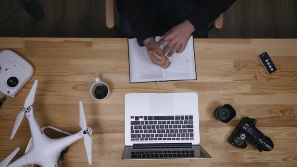 Top view of workplace photographer. A man working at the computer and drinking coffee. The items are laid out in the spirit of perfectionism on a wooden background — Stock Video