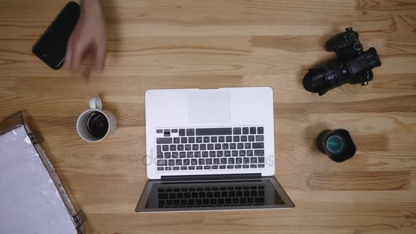 Vista superior del fotógrafo del lugar de trabajo. Un hombre trabajando en la computadora y bebiendo café. Los artículos están dispuestos en el espíritu del perfeccionismo sobre un fondo de madera — Vídeo de stock