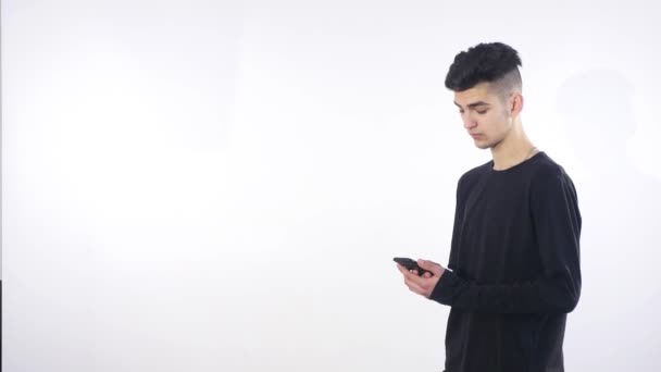 Joven sonriente mirando su teléfono inteligente mientras mensajes de texto aislados sobre fondo blanco — Vídeos de Stock