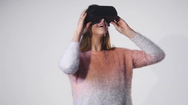 Hermosa joven atractiva en suéter rosa usando sus gafas VR. Fondo blanco aislado — Vídeos de Stock