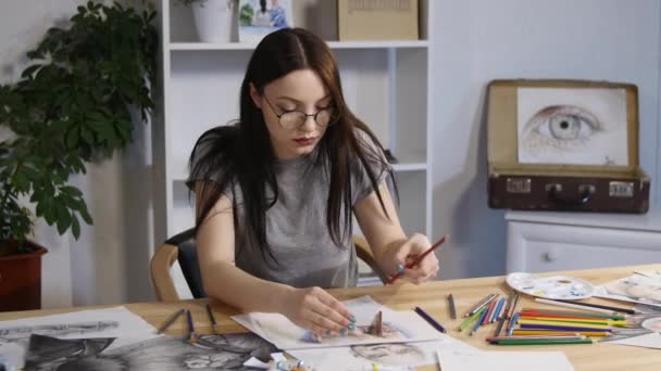 Привлекательная девушка в очках рисует портрет карандашами — стоковое видео