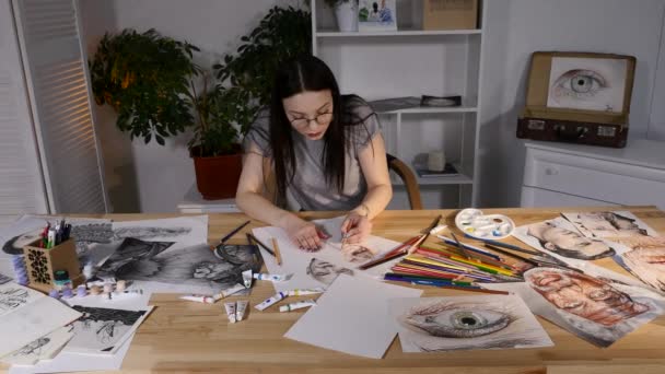 女性画家は、彼女のオフィスに座ってスケッチに取り組んでいます。彼女はメガネをかけて、 — ストック動画