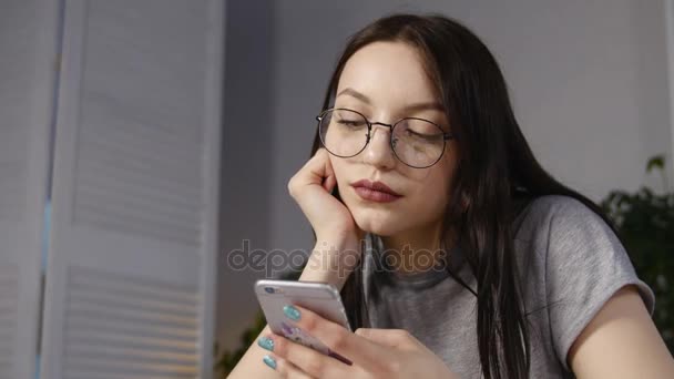 Junge Frau mit Brille, die Fotos auf dem Smartphone durchblättert. spiegelt sich in der Brille wider — Stockvideo
