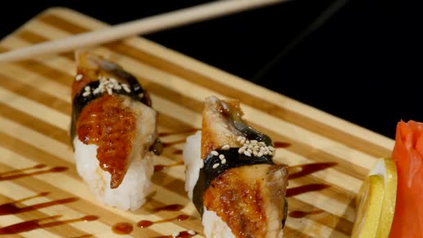 Rolos de sushi colocados em uma tábua de madeira de perto. girando no fundo preto — Vídeo de Stock