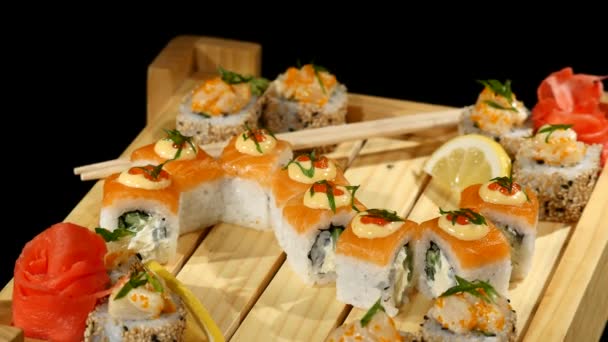 Rolos de sushi colocados em uma placa de madeira. girando no fundo preto — Vídeo de Stock