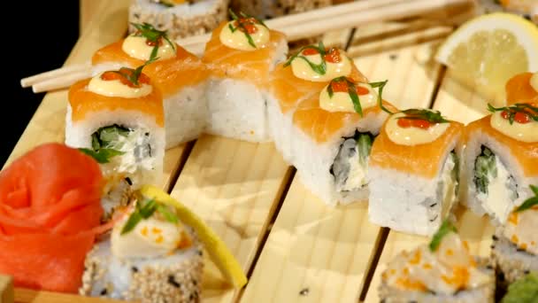 Los rollos de sushi colocados en una tabla de madera se cierran. girando sobre fondo negro — Vídeos de Stock