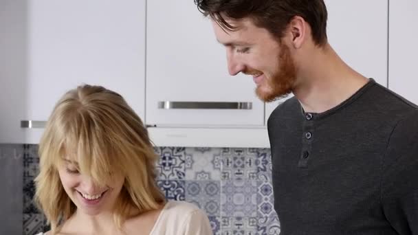 Milující přítelkyně krmení jeho usmívající se přítel kousek jablka v kuchyni — Stock video