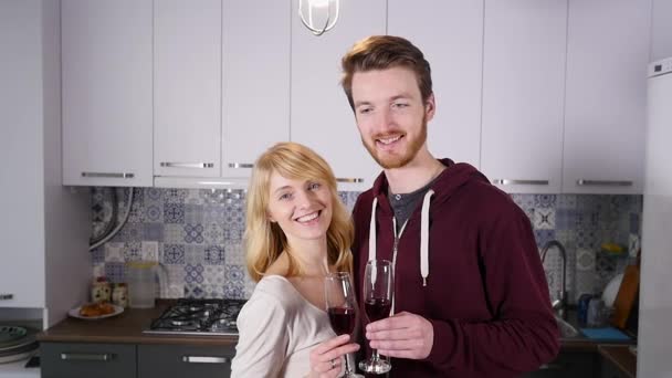 Νεαρό ζευγάρι πόσιμο κόκκινο κρασί στην κουζίνα στο σπίτι — Αρχείο Βίντεο