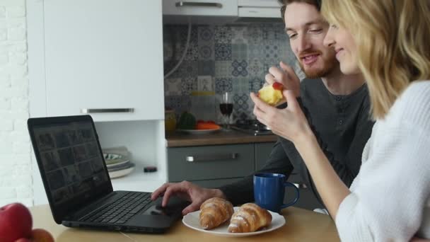 Pareja joven hablando por ordenador portátil durante el desayuno en la cocina — Vídeo de stock