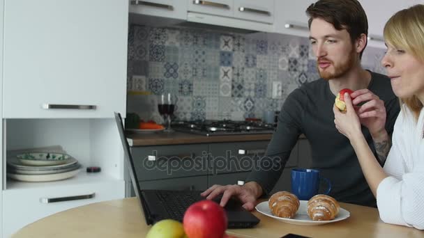 Giovane coppia che parla al computer portatile durante la colazione in cucina — Video Stock