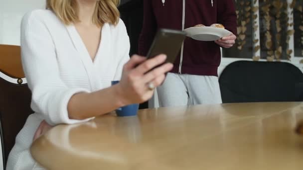 Beautiful woman sitting in kitchen, surfing Internet and having breakfast — Stock Video