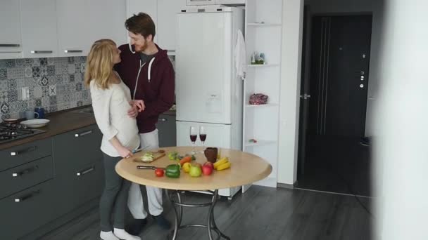 Любящий парень обнимает свою улыбающуюся подружку на кухне рано утром с завтраком, приготовленным в Slow Motion — стоковое видео