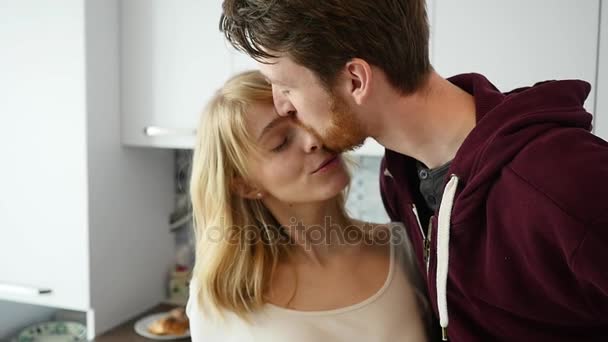 Tipo cariñoso abrazando a su novia sonriente en su cocina temprano en la mañana con el desayuno se hace en cámara lenta — Vídeos de Stock