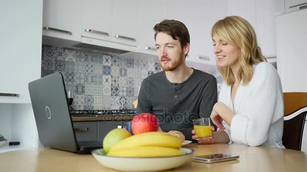 Casal jovem conversando sobre laptop durante o café da manhã na cozinha — Vídeo de Stock