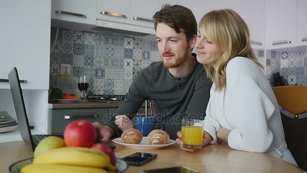 Fiatal pár beszél laptop reggeli közben a konyhában — Stock videók