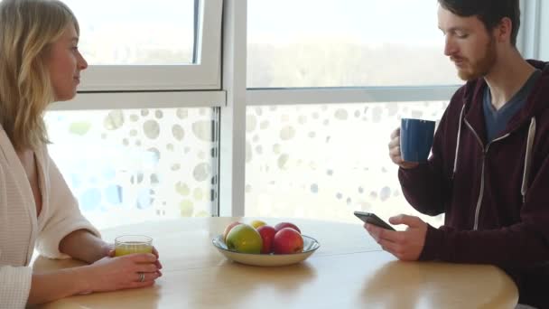 Casal jovem durante o café da manhã, homem mostrando algo no smartphone sua namorada — Vídeo de Stock