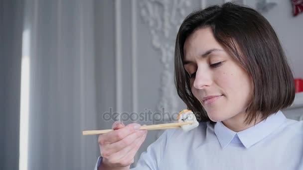 Beautiful young cheerful woman sitting at the table enjoying the taste of the sushi and smiling — Stock Video