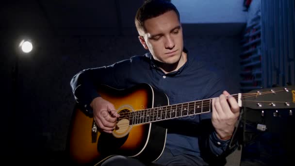 Joven tocando la guitarra acústica fondo oscuro en el estudio — Vídeo de stock