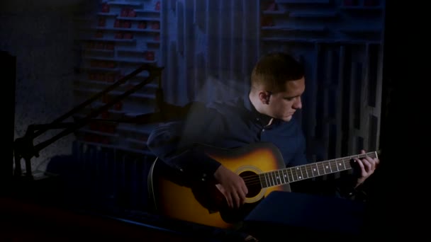 Jeune homme jouant de la guitare acoustique fond sombre en studio — Video