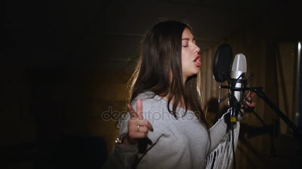 Jolie fille chantant dans le microphone du studio. La fille porte des écouteurs sur fond blanc. Dans la lumière basse du studio . — Video