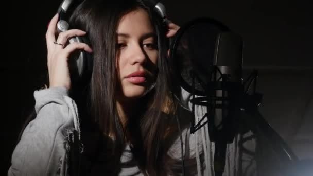 Young woman wearing headphones in recording studio near microphone — Stock Video