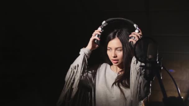 Young woman wearing headphones in recording studio near microphone — Stock Video