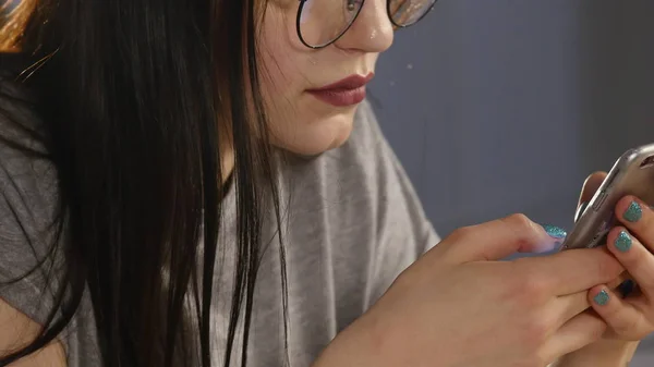 Young woman with glasses browsing photos on smartphone. reflected in the glasses — Stock Photo, Image