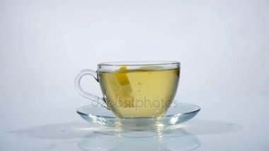 Bir fincan siyah çay bir fincan tabağı üzerinde yavaş mo, beyaz bir arka plan bir dilim limon düşüyor