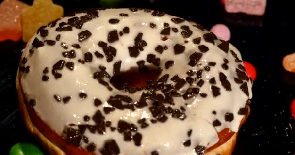 Белый глазурованный пончик с шоколадом, глазурью или брызгами, полосатые карамельные конфеты, красочный драже с изюмом или арахисом внутри на черном фоне — стоковое видео
