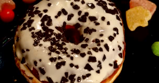 Donut vitrificado branco com chocolate, cobertura ou polvilhas, doces de caramelo listrado, dragee colorido com passas ou amendoins no interior sobre fundo preto — Vídeo de Stock