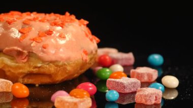 Turuncu komik sürpriz sırlı çörek ile sprinkles, çizgili karamelli şeker, Kuru üzüm veya fıstık içinde renkli badem döndürmek siyah arka plan üzerine