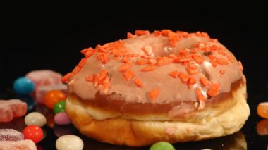 Turuncu komik sürpriz sırlı çörek ile sprinkles, çizgili karamelli şeker, Kuru üzüm veya fıstık içinde renkli badem döndürmek siyah arka plan üzerine