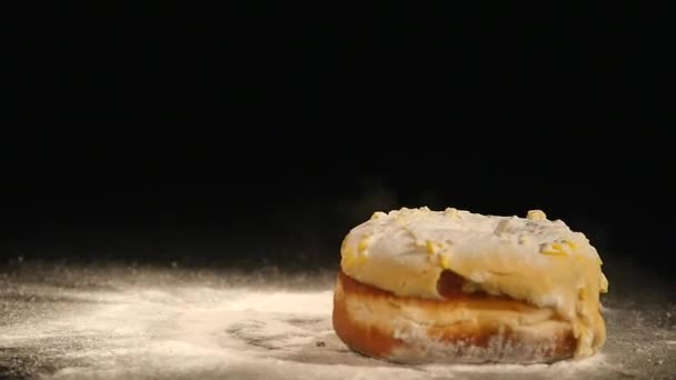 Un beignet avec une poudre de sucre tombe sur un bureau noir — Video