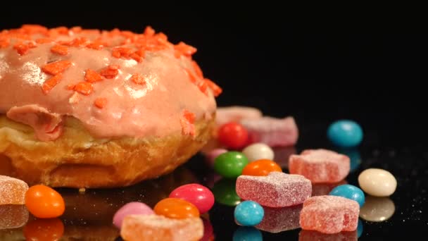 Laranja engraçado surpreendido donut envidraçado com polvilhas, doces de caramelo listrado, dragee colorido com passas ou amendoins dentro girar sobre fundo preto — Vídeo de Stock