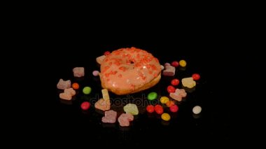 Turuncu komik sürpriz sırlı çörek ile sprinkles, çizgili karamelli şeker, Kuru üzüm veya fıstık içinde renkli badem döndürmek siyah arka plan üzerine