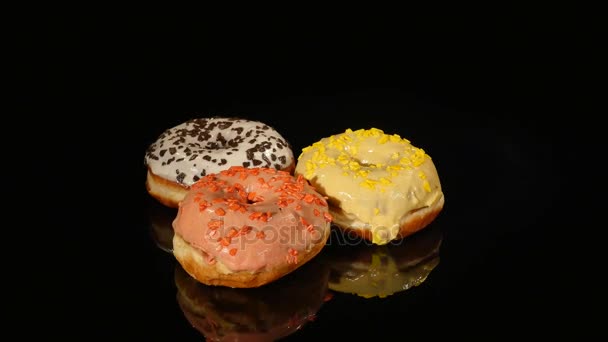 Donuts vitrificados com diferentes recheios giram sobre um fundo preto — Vídeo de Stock