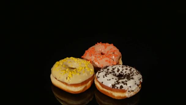 Donuts vitrificados com diferentes recheios giram sobre um fundo preto — Vídeo de Stock