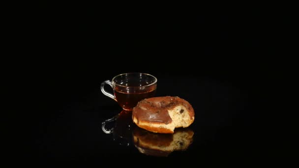 Copos de chá e donuts de chocolate giram sobre um fundo preto — Vídeo de Stock