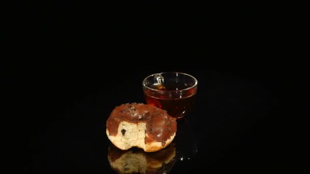 Чашки чаю та шоколадних пончиків обертаються на чорному тлі — стокове відео