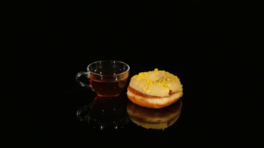 Bardak çay ve çörekler sarı sır ile siyah bir arka plan üzerinde döndürme